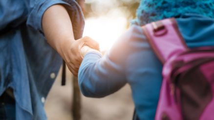 Two people help each other on a hike and hold hands supportively.