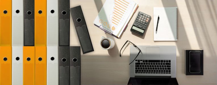 A desk with work utensils, such as a folder, laptop, pad and pen.