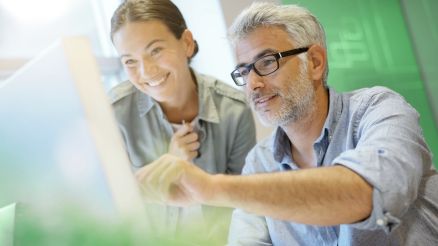 A man and a woman look at information on a notebook.