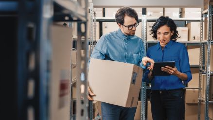 A man and a woman look at inventory on a tablet in a warehouse.