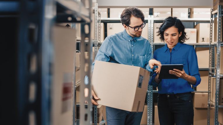 A man and a woman look at inventory on a tablet in a warehouse.