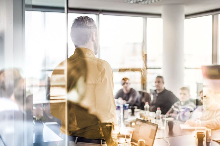 A business situation in a conference room where a speaker is standing in front of a team.