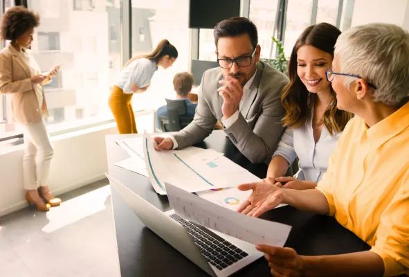 Ein Business Team schaut sich Analyseergebnises auf einem Laptop und Papier an.